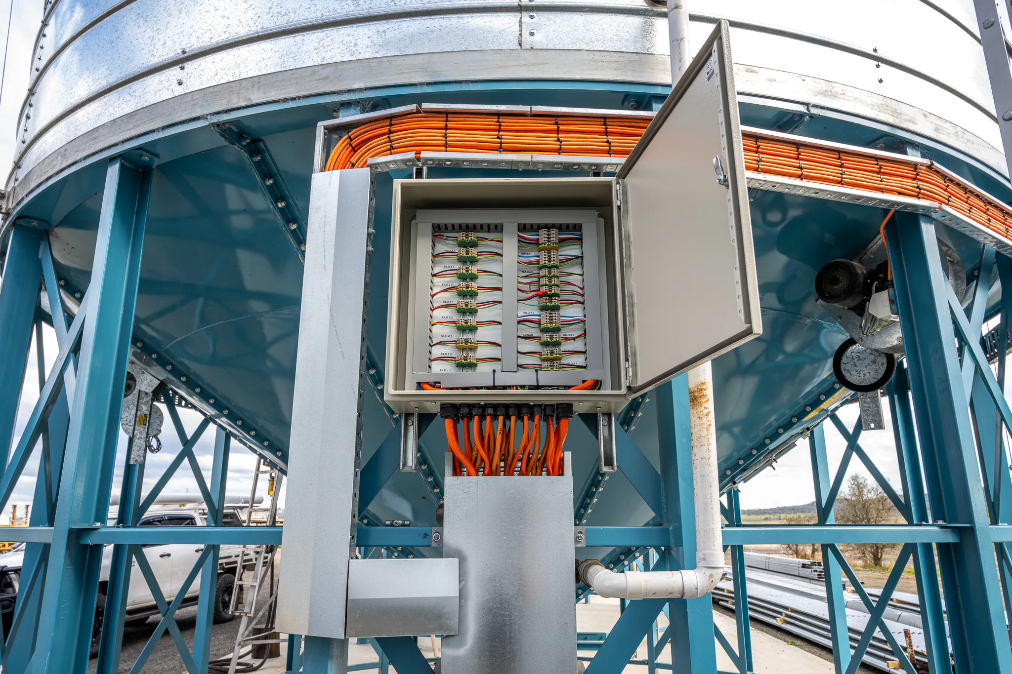 An open field-wiring enclosure with labelled terminal strips and orange sensor looms landed at a grain silo