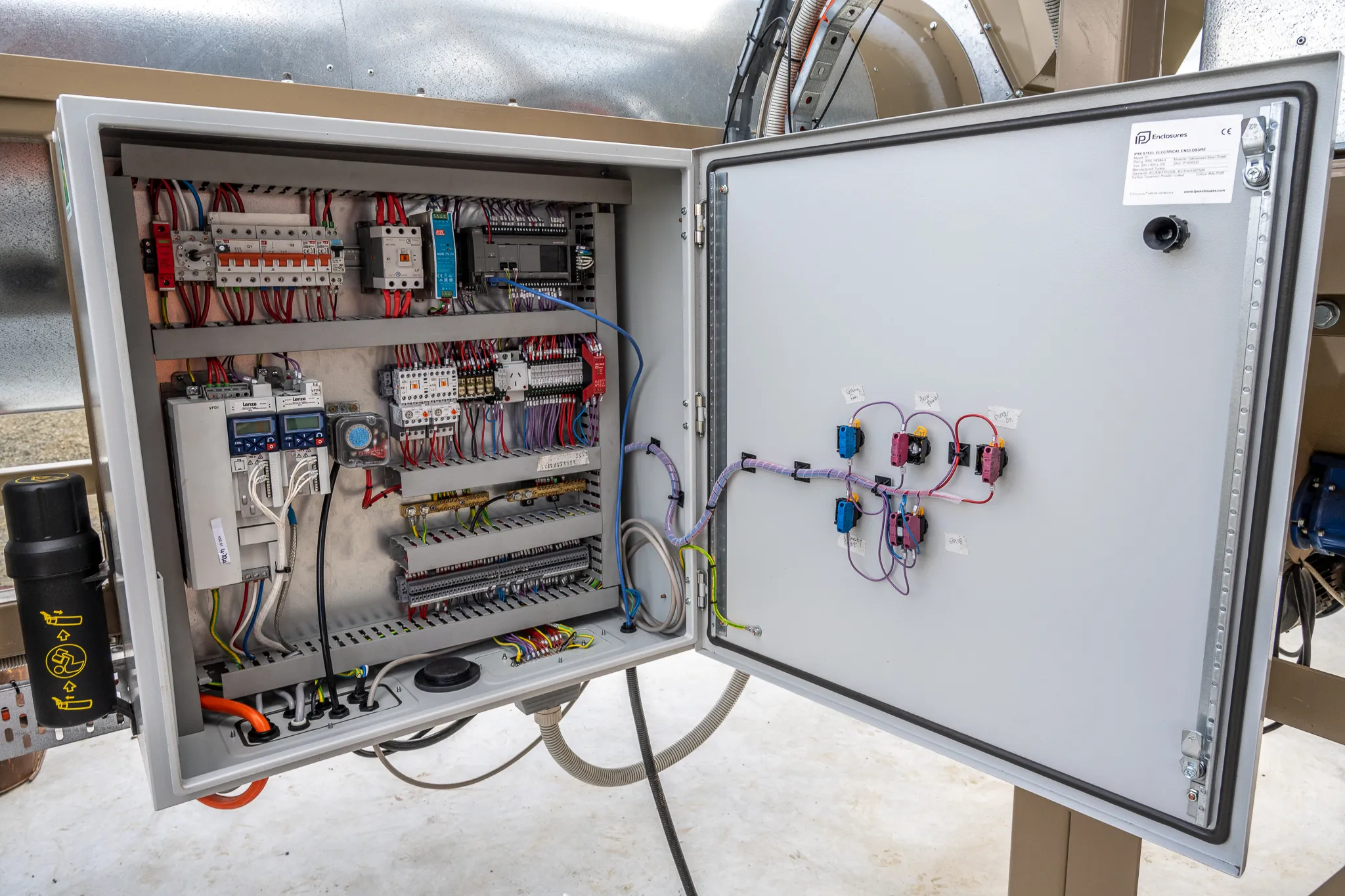 An open Switch'D-built control cabinet with variable-speed drives, a PLC, contactors and labelled door controls