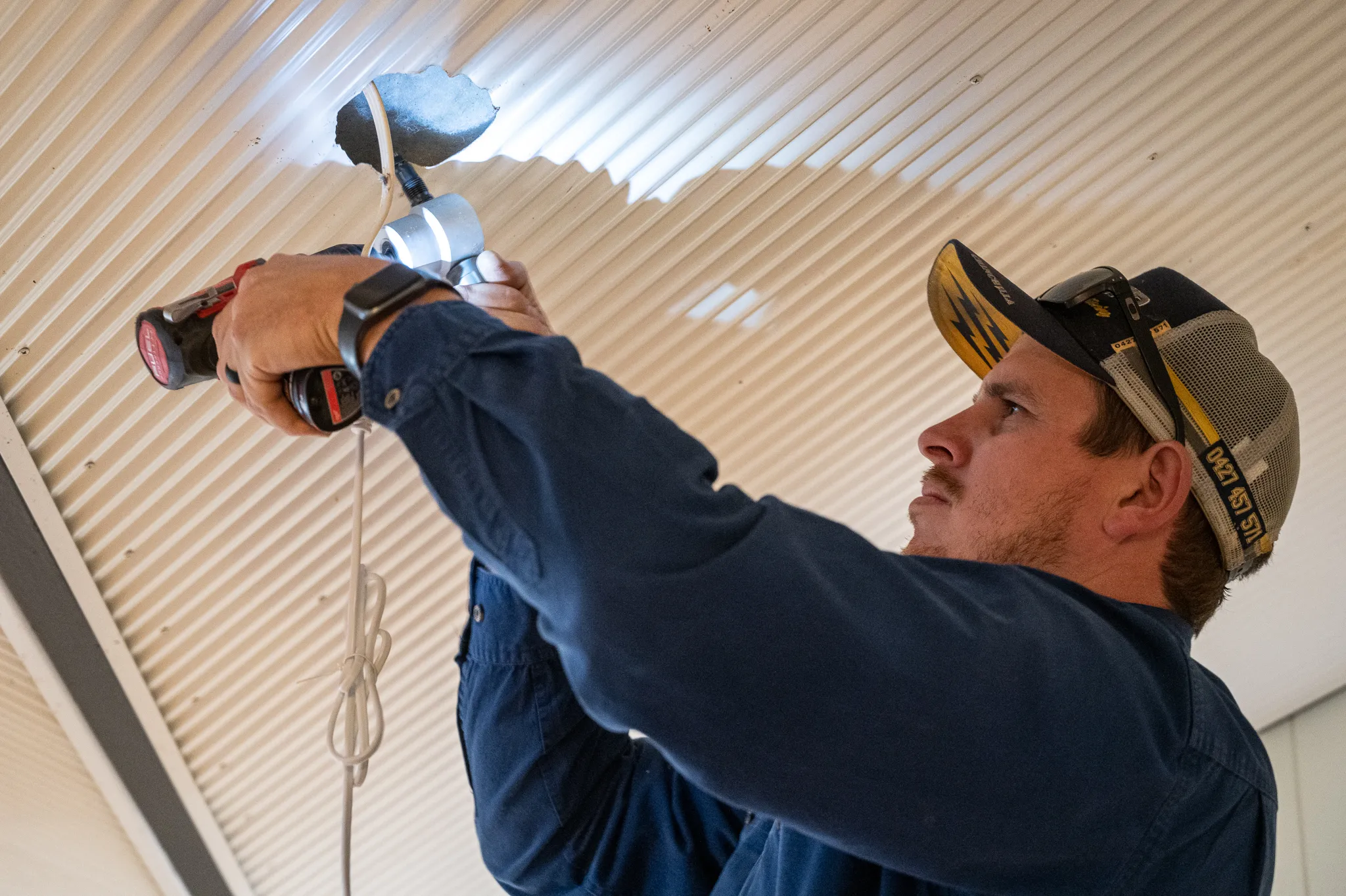 A Switch'D electrician fitting a light and fan mount to a corrugated patio ceiling