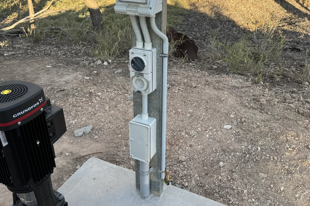 A vertical multistage bore pump and stainless control pillar on a concrete pad in the scrub.