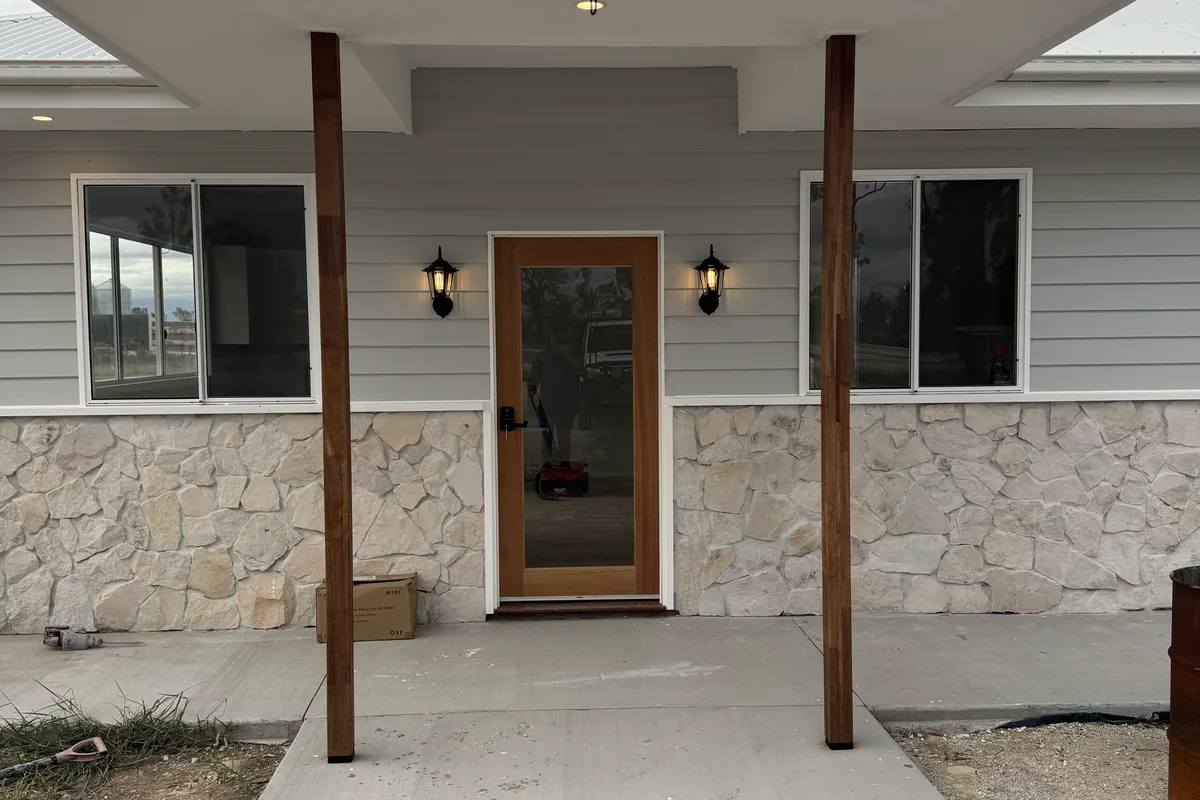 The front porch of a new home with timber posts, a stone base and coach lights either side of the door.