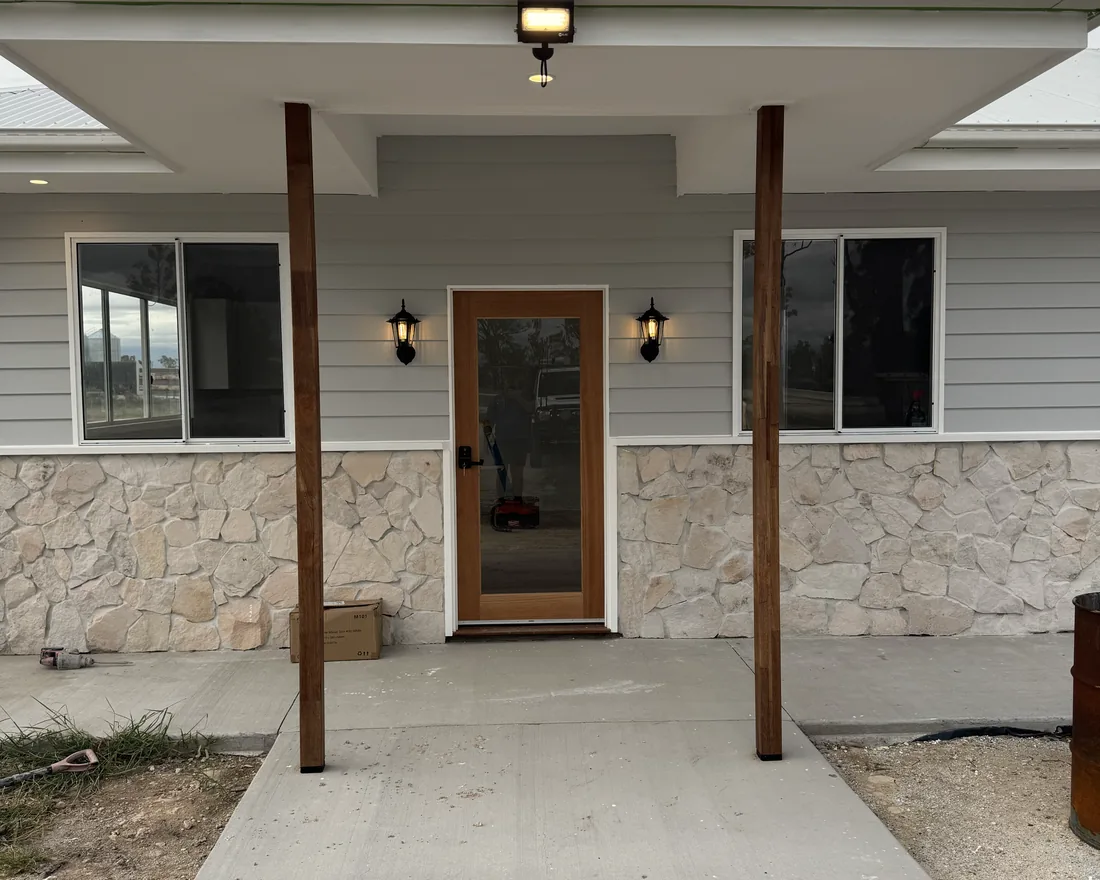 The front porch of a new home with timber posts, a stone base and coach lights either side of the door
