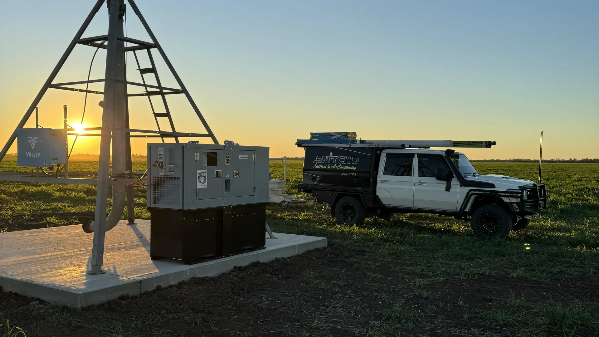 Centre-pivot tower silhouetted against the setting sun, with the generator and control cabinet installed on a new concrete pad