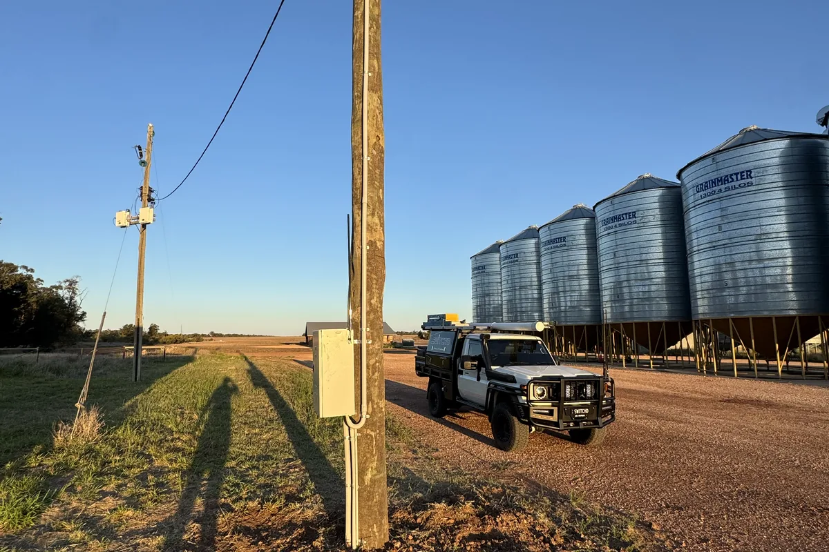 A timber power pole and meter enclosure with a row of grain silos and the ute behind.