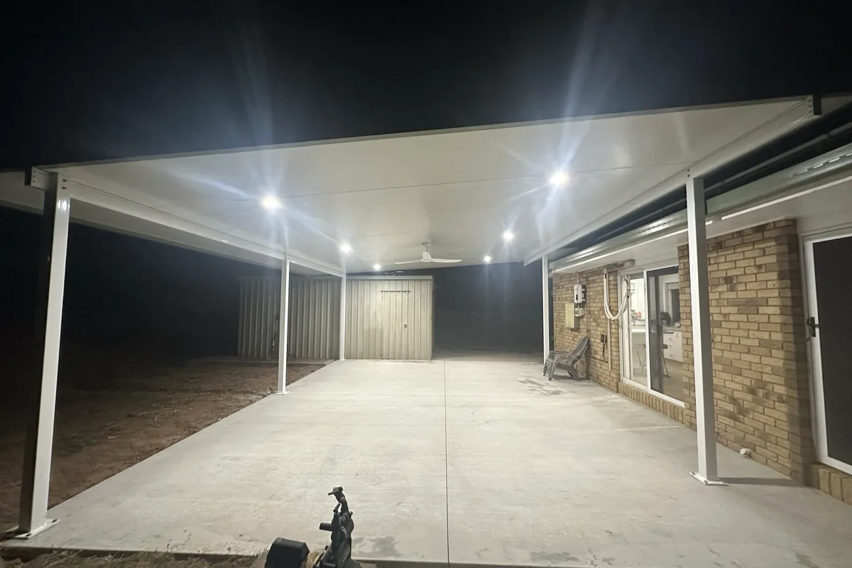 A new attached patio and carport lit end to end by downlights and a ceiling fan after dark, with the shed behind.
