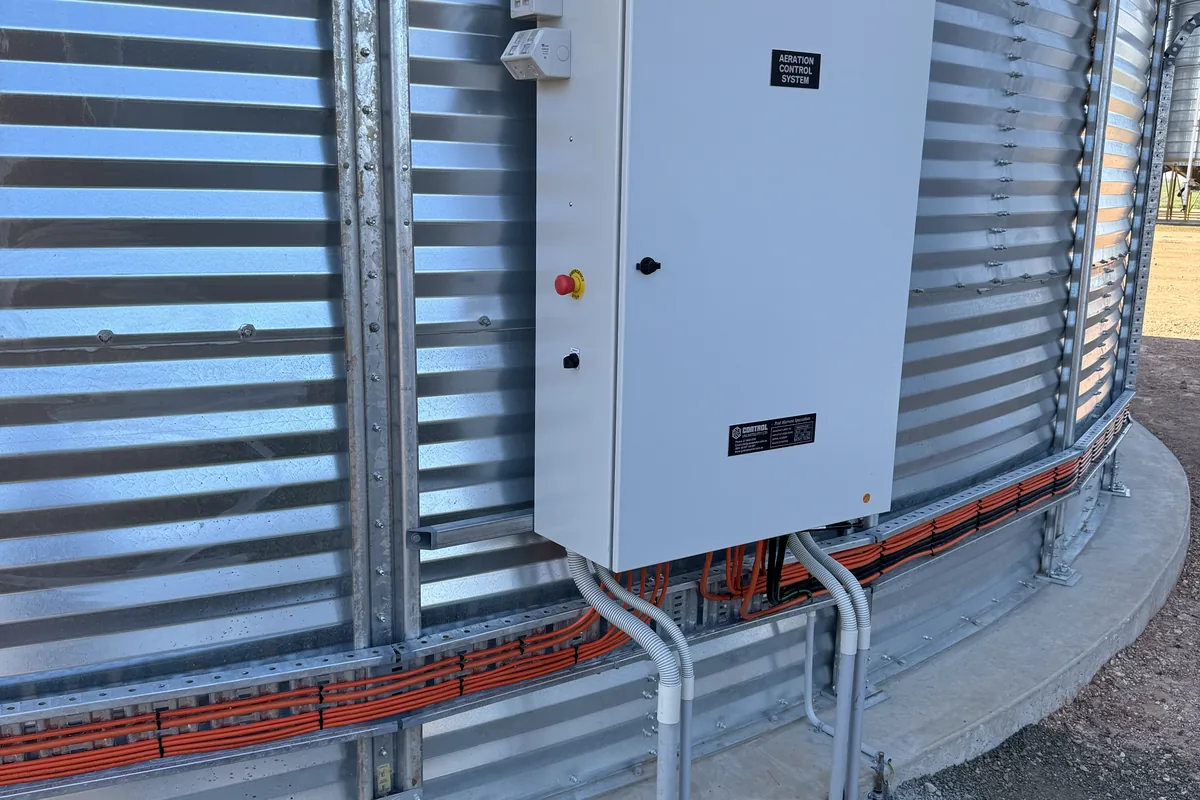 A white aeration control box on a galvanised silo wall with conduit run down to the base.