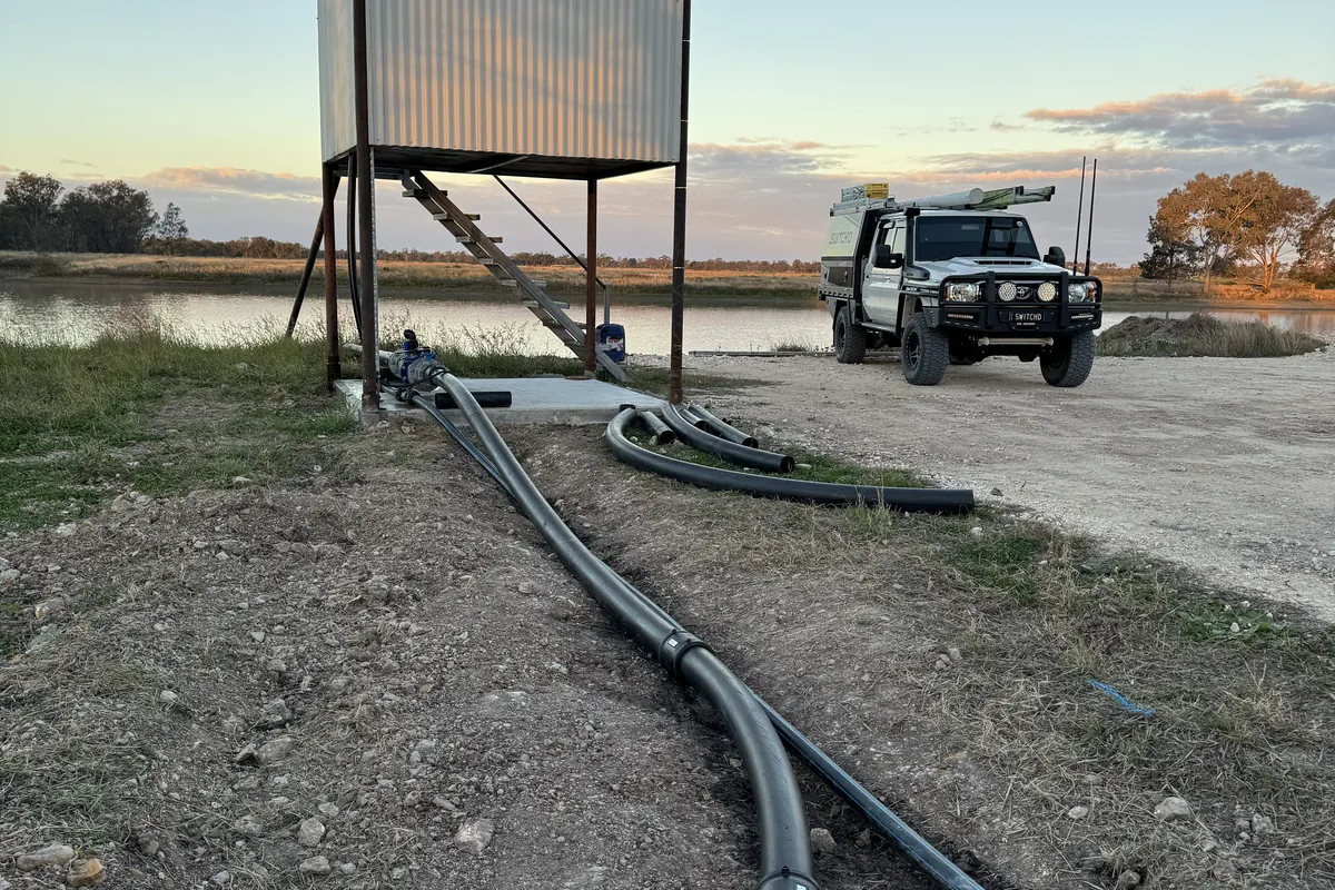 An elevated water tank with poly pipe run to a dam and the ute alongside at sunset.